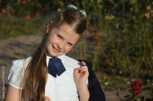 A beautiful girl with long hair in a school uniform, white shirt, holding a jacket in her hand. standing in the park. background for the design.