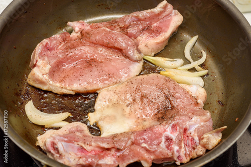 Marinated meat is fried with onions and vegetable oil in a frying pan.
