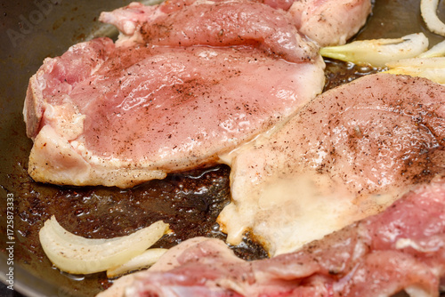 A close-up of marinated meat being fried with onions and vegetable oil in a frying pan.