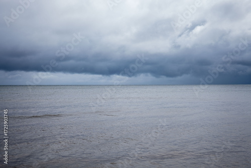 Dark clouds gather over the calm sea on a quiet afternoon, creating a serene yet dramatic atmosphere in the coastal landscape
