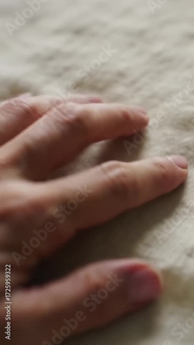 A clean, gender-neutral hand gently strokes pristine organic cotton fabric, captured in an extreme close-up video with soft natural light and a blurred bokeh background, enhancing its tactile