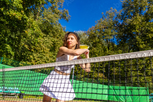 Focused female tennis player leaning on the net with yellow racket on sunny outdoor court