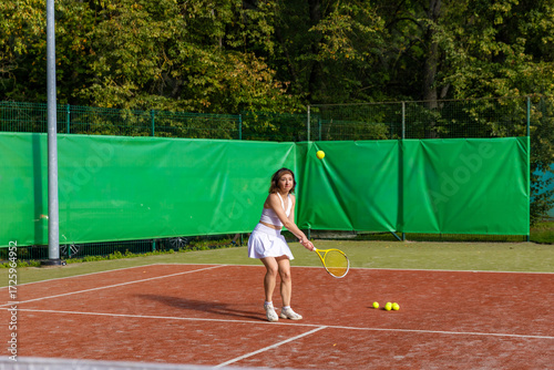 Young woman tossing the ball before serving with backhand grip on clay tennis court