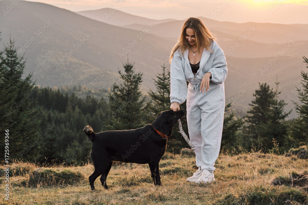 © KatyaPulka - A young woman enjoys playing with her dog in a beautiful mountain setting at sunset. The scenery adds to the happy, relaxed mood of the scene. Captured in warm, natural light.
