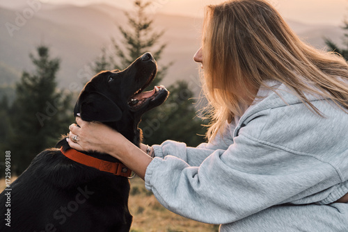 A loving moment shared between a woman and her black Labrador Retriever in a scenic outdoor setting. Showcasing companionship and the bond between humans and animals.