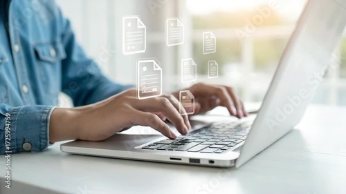 Person typing on a laptop with document icons floating above the keyboard on a white table top view