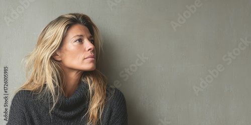 Contemplative Woman with Long Hair in a Cozy Sweater Against a Neutral Background