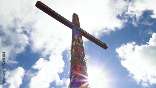 A wooden cross stands tall against a backdrop of blue sky and white clouds