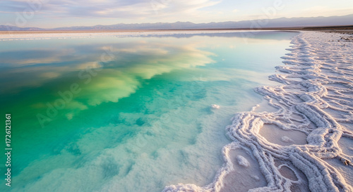 Vibrant Turquoise Water Reflecting Clouds Meeting Ornate White Salt Shoreline
A stunning and vibrant landscape featuring the crystal-clear, shallow water of a salt lake or lagoon
