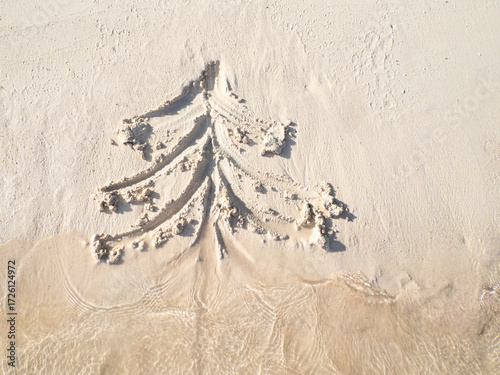 a Christmas tree painted on the sand of the beach and sea waves