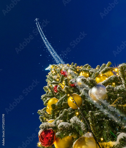 Airplane flies up to the dark blue sky and leaving a trail using the decorated christmas fir tree as the launching platform or the runway
