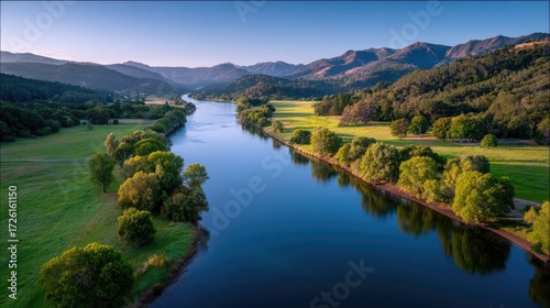Scenic River Valley at Sunrise with Towering Mountains Lush Greenery and Golden Sunlight Casting a Warm Glow on the Water and Surrounding Landscape