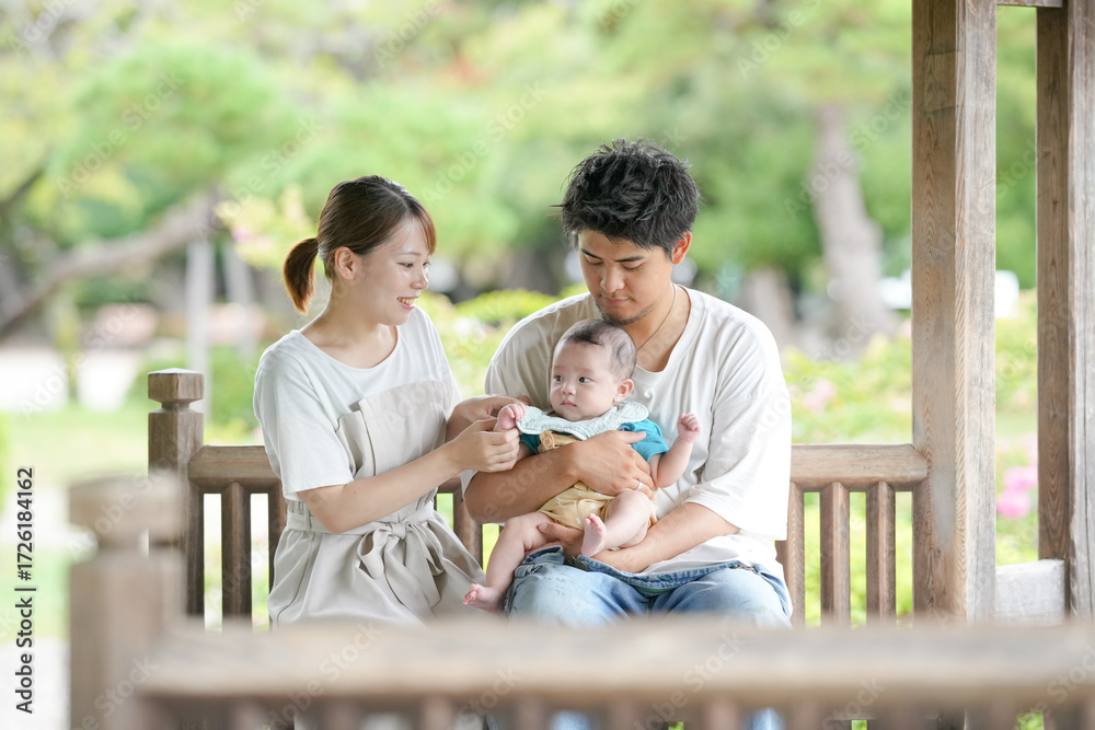 Fototapeta premium A man and a woman are holding a baby on a bench. The baby is wearing a blue shirt