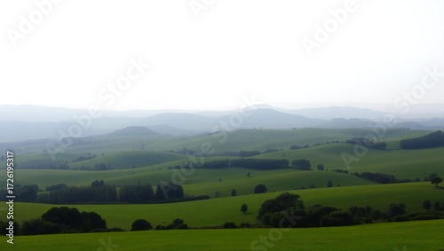 Misty rolling green hills and distant mountains under a hazy sky