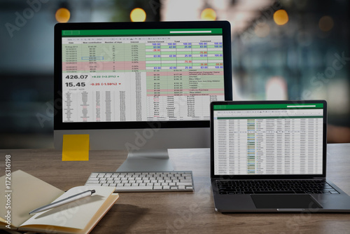Fotografie Desktop monitor and laptop display a detailed spreadsheet with financial figures