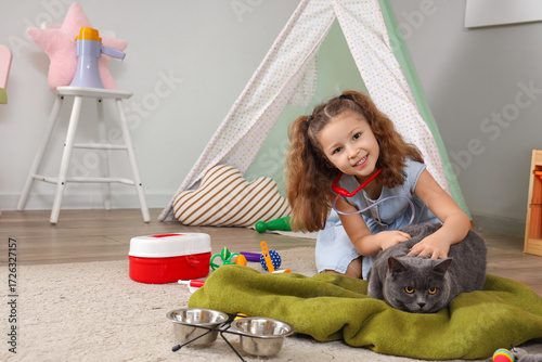 Cute little girl with first aid kit examining British cat at home