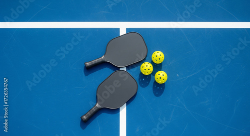 Black pickleball paddles and balls on a blue court, overhead view
