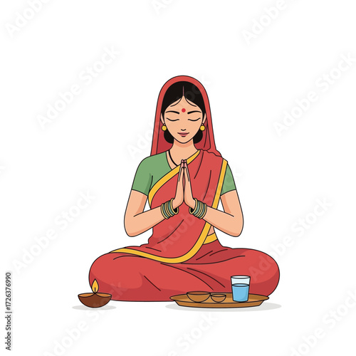 Woman in sari meditating in lotus position with prayer hands, lamp, water and offering.