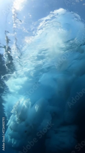 Cinematic video descends from a colossal iceberg tip in azure arctic waters, revealing its immense, luminous underwater mass with god rays. Concept of unseen power and potential