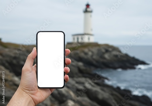 A person holding a smartphone with a blank screen, lighthouse in the background.