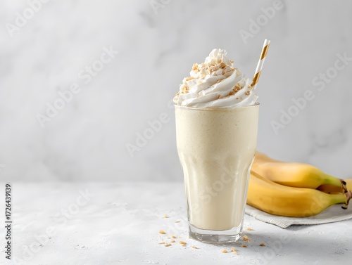 Banana milkshake with whipped cream on top, white surface, and open space above for slogan or branding..