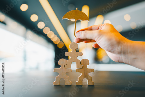 Obraz na plátne Hand holding umbrella icon over wooden human figures in pyramid shape, symbolizing insurance protection, family care, team safety, risk management, and employee welfare concept