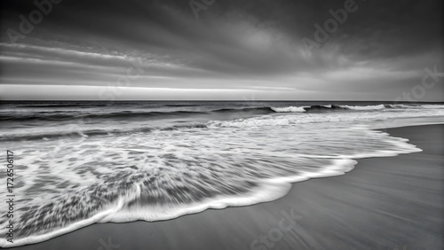 A black and white image of a beach with waves crashing on the shore under a cloudy sky at dusk or dawn