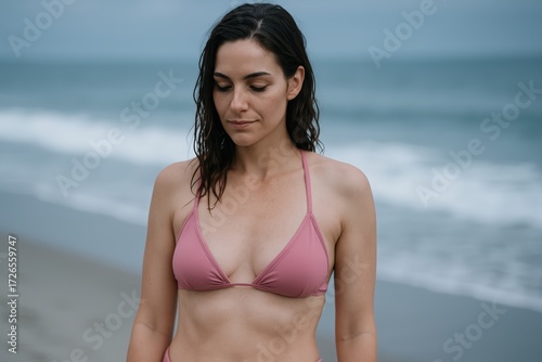 Young Woman Wearing Pink Bikini Top Standing on Beach with Ocean in Background