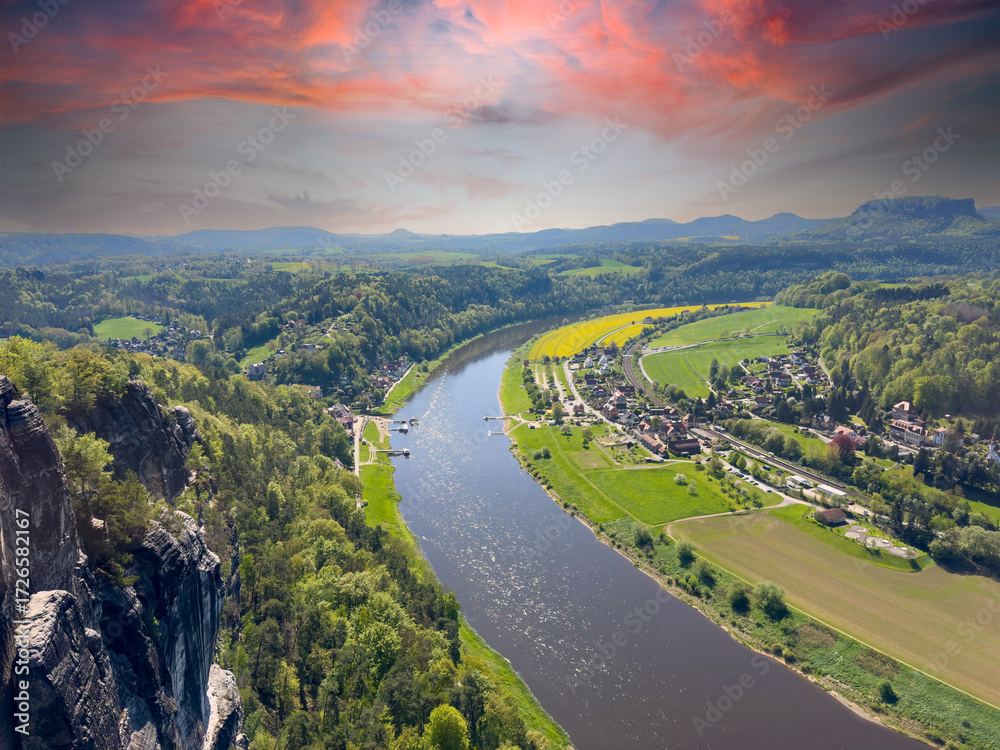 Fototapeta premium aerial view of rural village rathen in the elbe sandstone mountains in east germany with the river elbe from the bastei area with sunset
