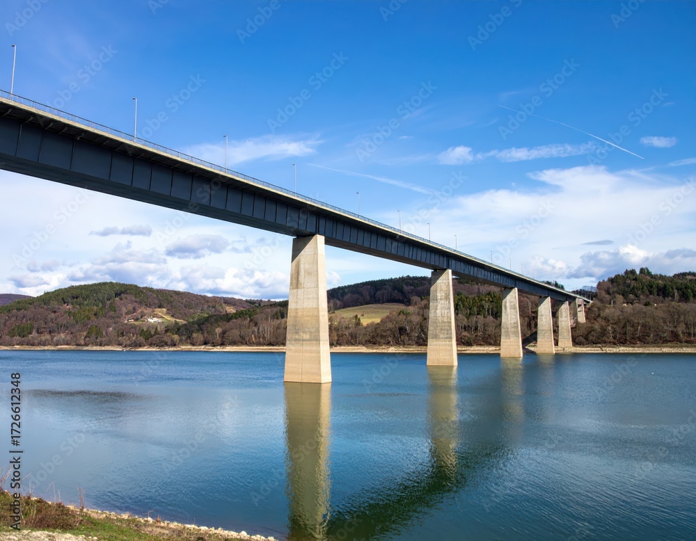Fototapeta premium Modern bridge spanning a large lake with calm reflections under blue sky