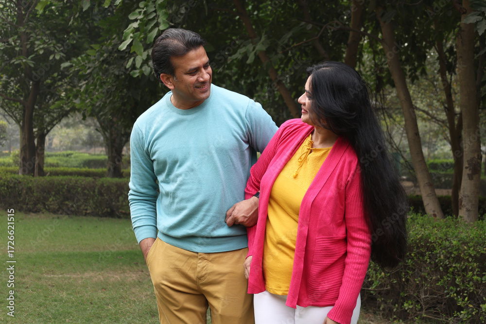 Obraz premium Indian happy young couple standing and looking each other with love and care. Indian Smiling young couple holding hands and standing outdoors at the nature. Celebrate the form of love at park