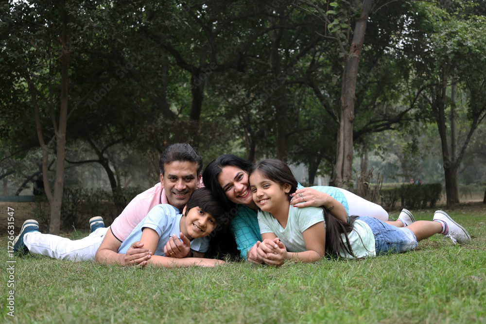 Fototapeta premium Happy Indian family spending leisure time at the nature outdoor park. Happy indian couple with kids embracing by looking at camera at garden. Concept of relationship, togetherness and family lifestyle