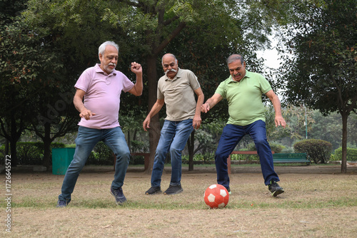 Active Indian senior friends playing football in garden