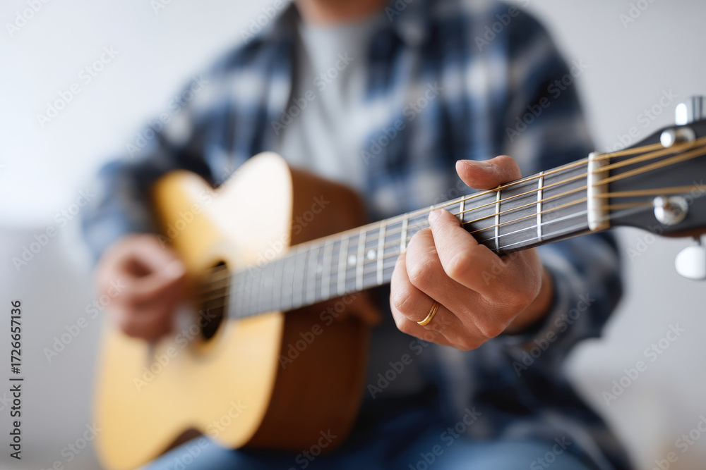 Fototapeta premium Acoustic guitar player strumming wooden instrument with fingers, wearing casual plaid shirt, creating warm and relaxed music atmosphere