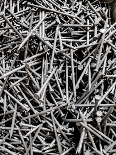 Pile of shiny new nails scattered randomly, creating a textured industrial pattern with a metallic sheen, showcasing strength and construction, in a closeup shot.