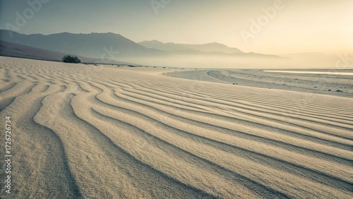 Sand ripples create a calming landscape in a desaturated desert at dawn near a distant mountain range