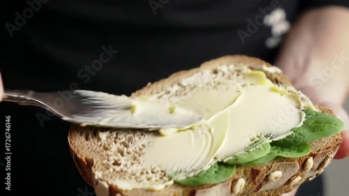 Close up shot of a persons hands using a knife to spread yellow butter or margarine on a slice of healthy whole grain seed bread for a delicious sandwich.