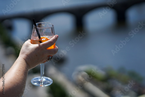 Woman holding spritz cocktail drink with orange above river, close-up view