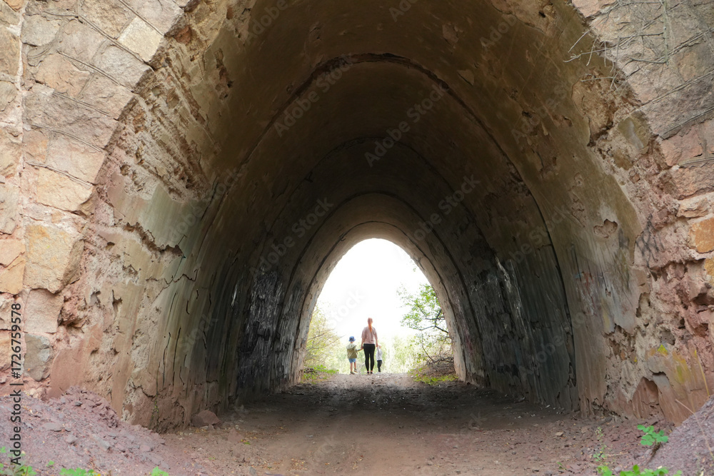 Obraz premium 4K video of a mother with two little boys walking into a stone tunnel on a forest path. Concept of family travel, childhood adventure and exploration of nature