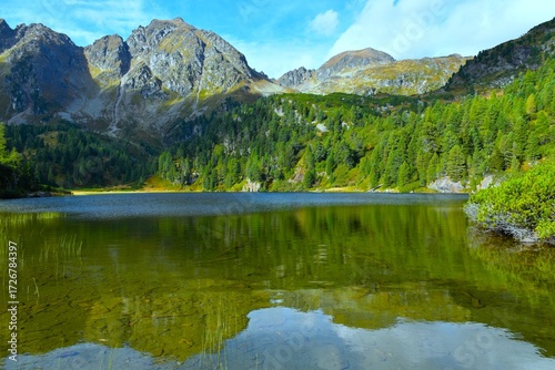Reflection of the the mountains aove in the water of Zwiefler lake with conifer trees above the lake in Sölktäler nature park Niedere Tauern, Styria, Austria