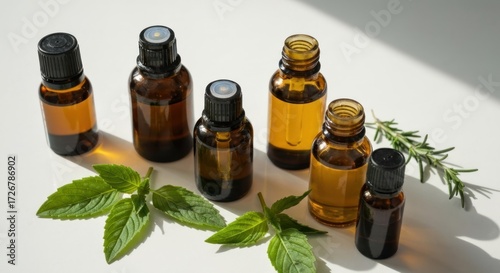 Amber glass bottles of essential oils arranged on a white surface with fresh mint and rosemary sprigs. Sunlight casts soft shadows