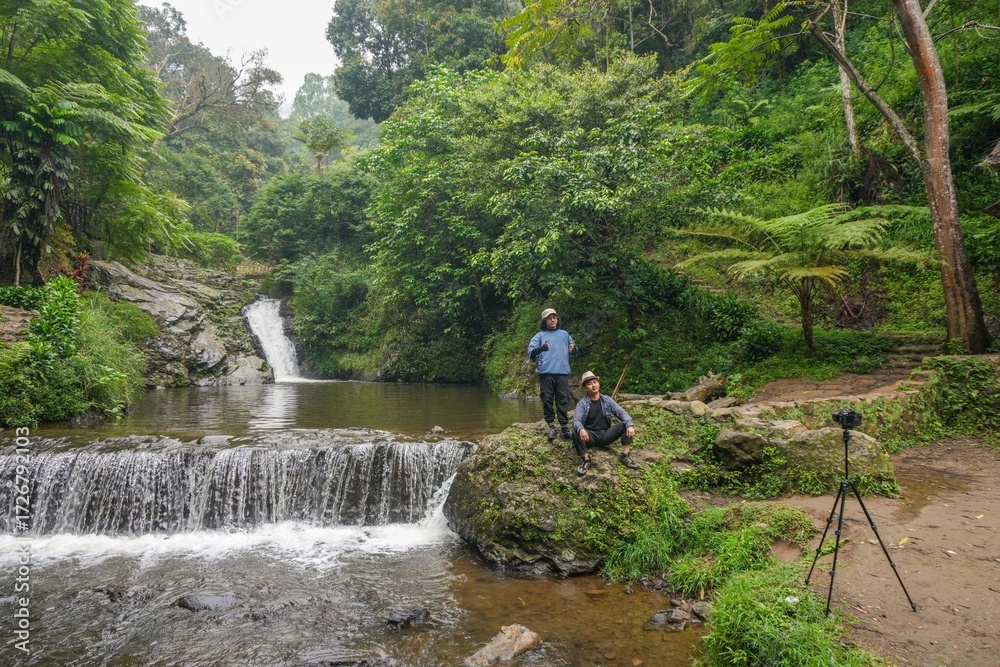 Fototapeta premium Two Adventurous Friends Capturing Moment While Explore Lush Jungle Waterfall