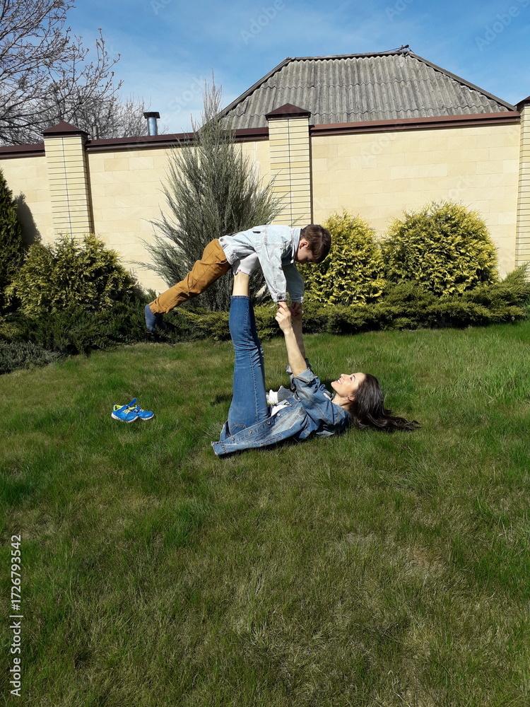 Fototapeta premium Young caucasian mother and son playing on grass in backyard on sunny day