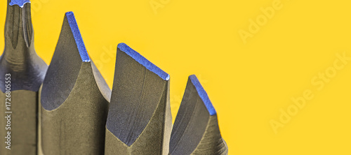 Macro photograph of various screwdriver bits with sharp metallic edges on yellow background. The detailed image emphasizes the industrial design and precision of the tool heads. Selective focus.