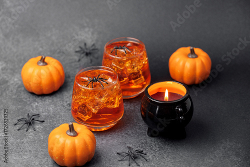 Orange pumpkin drinks with spiders and lit cauldron candle on dark background.