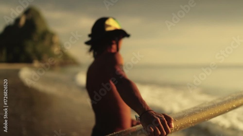 Young Man walking in a Swimsuit Holding Surfboard Walks on the Beach Towards the Sea