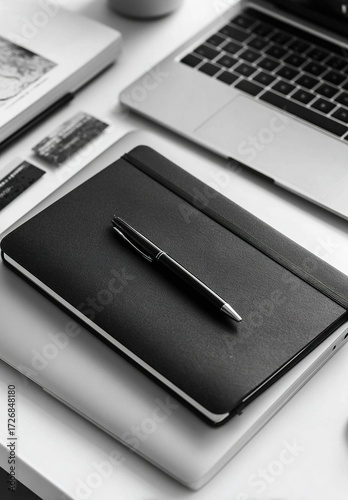 Black notebook on white desk with business card holder and laptop

