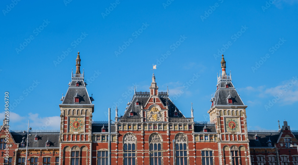 Fototapeta premium Central Station in Amsterdam, Netherlands, showcasing its neo-Renaissance architectural style with intricate details, spires, and decorative elements under a clear blue sky.