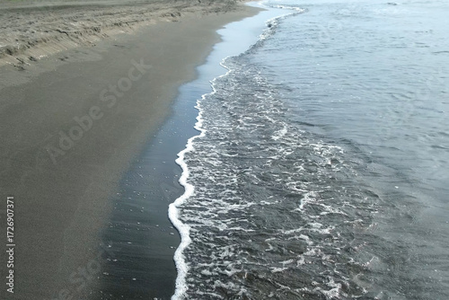 Gentle waves washing sea shore with sandy sand volcanic beach., creating tranquil ambiance with gentle rippling against coastal landscape during peaceful summer day. Wonderful wild nature landscape.