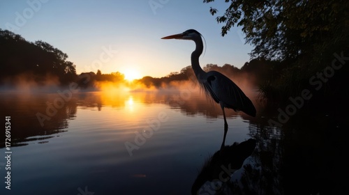 Great blue heron silhouette stands serenely amidst a hazy golden sunrise over reflective water
